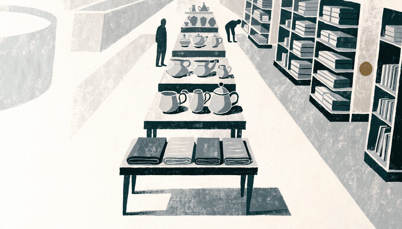 Editorial illustration of a department store gift-and-lifestyle floor: tiered display tables of tableware and folded textiles recede down a long aisle beside shelving, with two silhouette figures browsing, in a near-monochrome grey and ink palette with one small brass-gold accent.